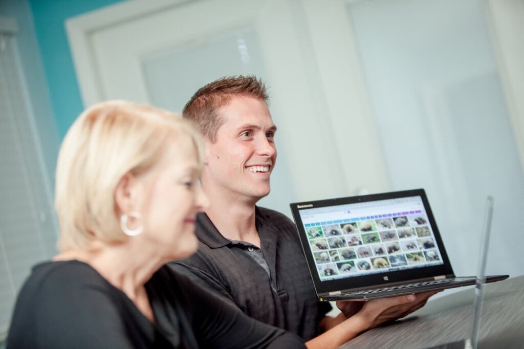 A woman and a man displaying a screen from a laptop.