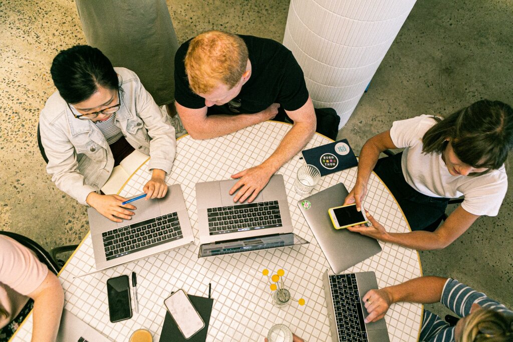 Overhead view of a team collaborating around a table with laptops and phones.