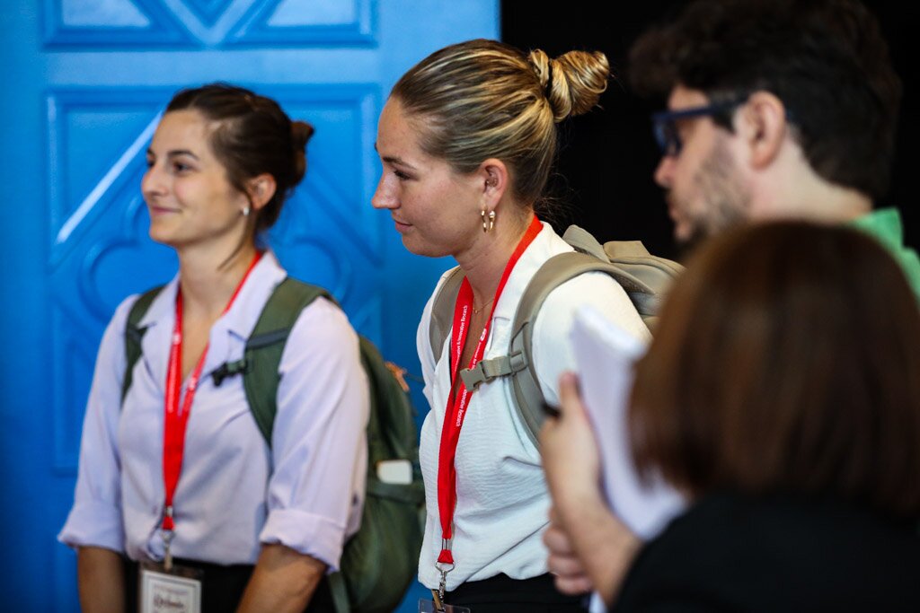 Attendees with backpacks and conference lanyards listening during a session.