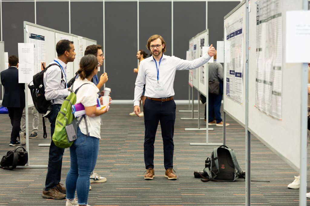 A presenter explaining his research poster to attendees at a poster session.