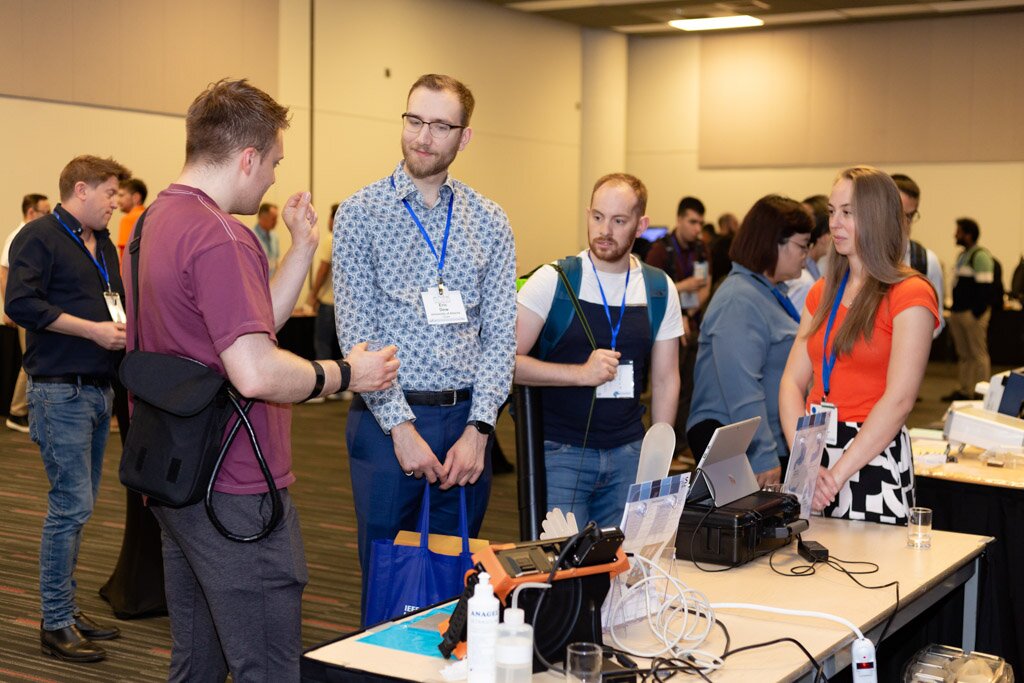 Attendees talking at an exhibit table with equipment on display.