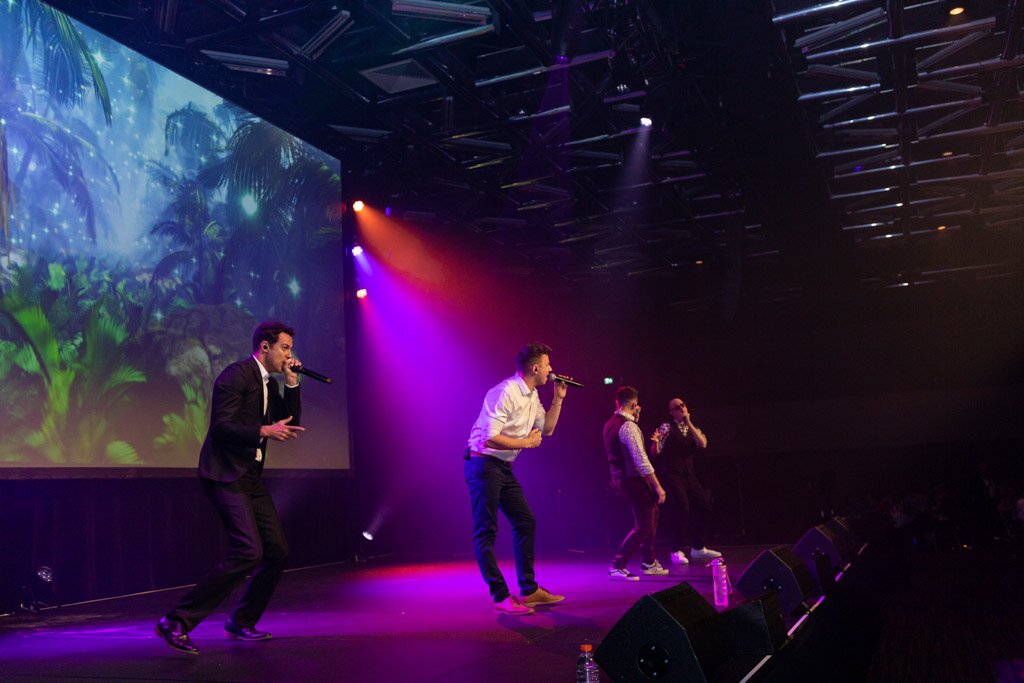 A vocal group performing on stage under purple lights.