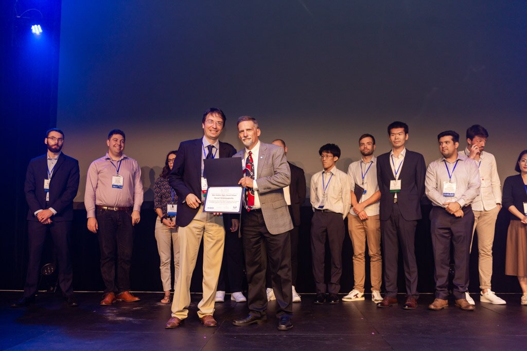 An award being presented on stage as a group of honorees looks on.