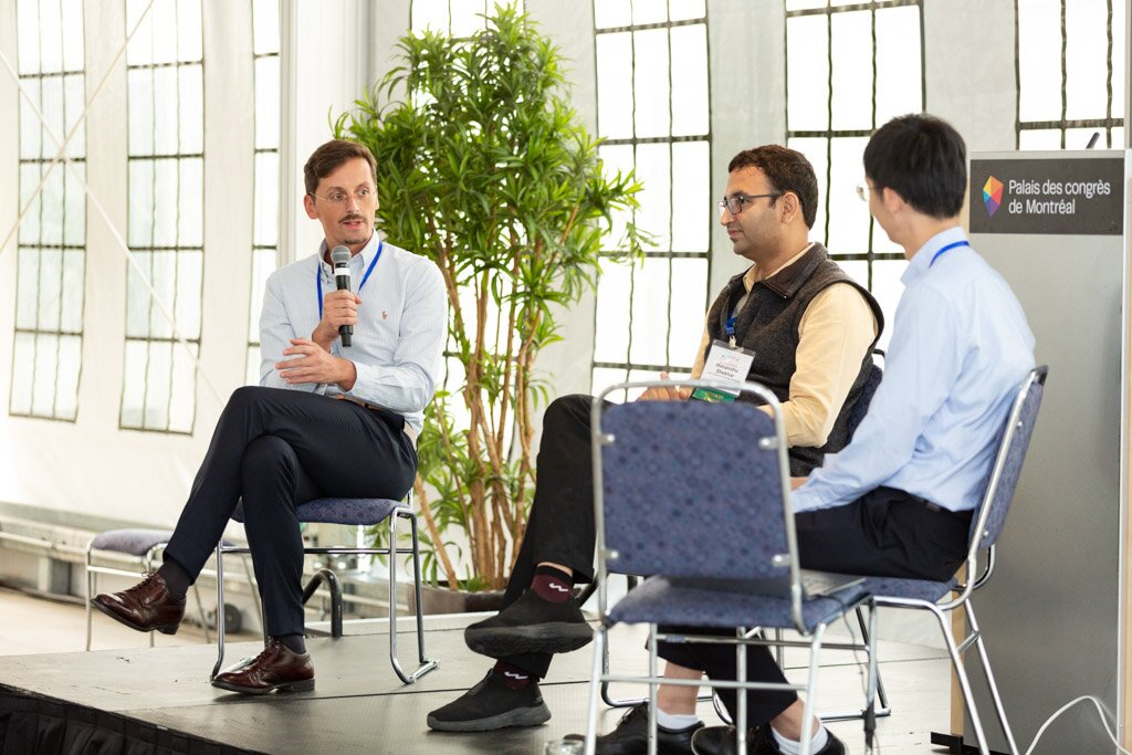 Three panelists in conversation on stage during a conference session.