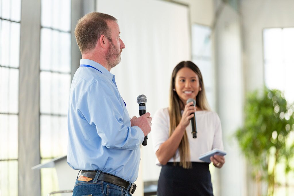 A moderator and a presenter with microphones on stage.