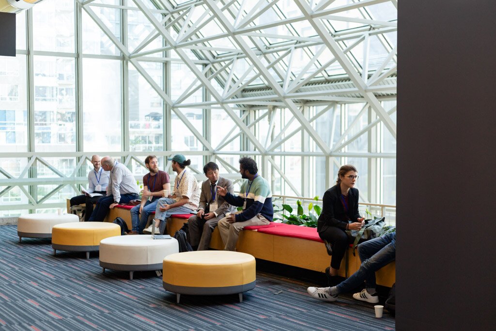 Attendees talking and relaxing in a glass-walled convention center lounge.