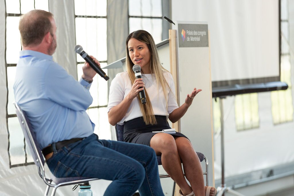 A moderator and a panelist speaking into microphones during an on-stage conversation.