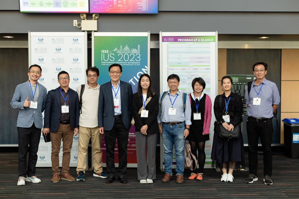 A group of attendees posing in front of IEEE IUS 2023 banners.