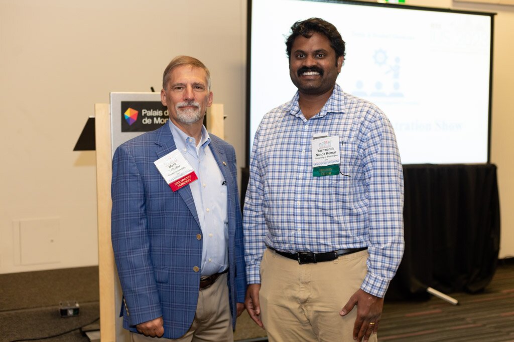 Two men posing in front of a presentation screen at a conference.