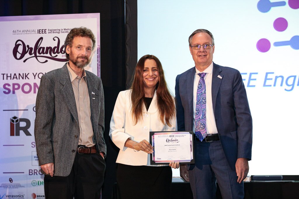 A woman holding an award certificate between two men on stage at a conference.