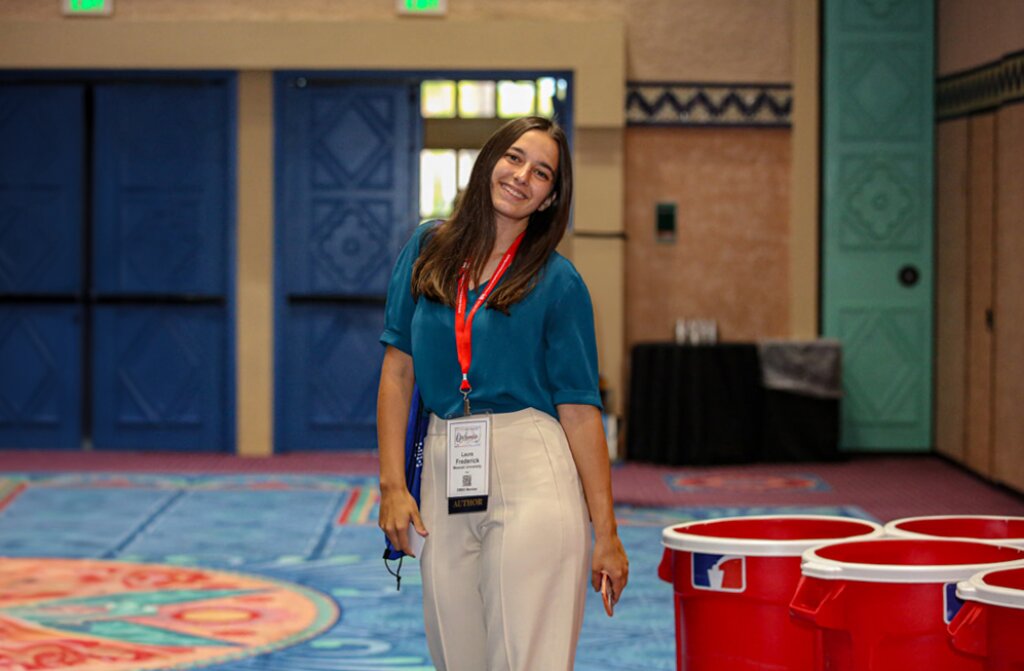 A smiling attendee posing in a colorful convention center hall.