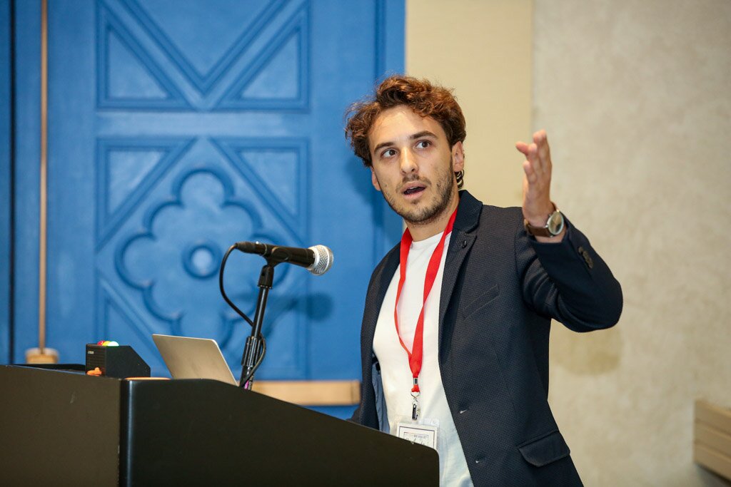 A young man presenting at a podium and gesturing to the audience.