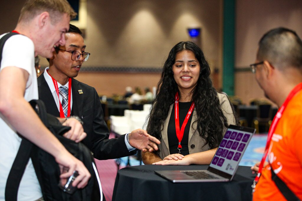 Attendees gathered around a laptop at a cocktail table during a conference.